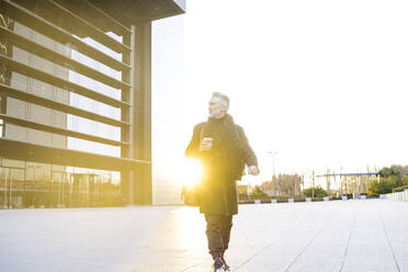 Geschäftsmann mit Kaffeetasse auf dem Fußweg bei Sonnenuntergang - JJF00743