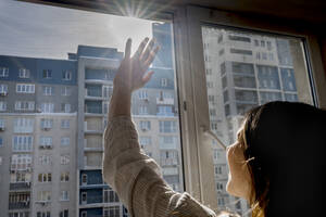 Frau, die ihre Augen abschirmt und durch ein Fenster in die helle Sonne schaut - ANAF01089