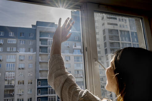 Woman shielding eyes looking at bright sun through window - ANAF01089