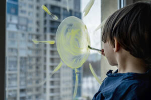 Junge zeichnet Sonne auf Glas mit Pinsel - ANAF01099