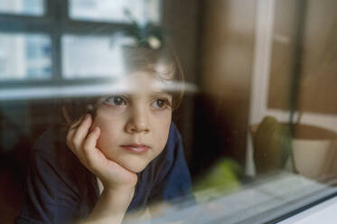 Nachdenklicher Junge schaut durch ein Glasfenster - ANAF01104