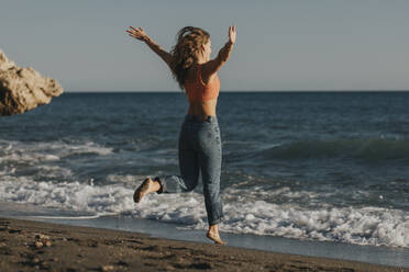 Frau springt an einem sonnigen Tag vor das Meer - DMGF01091