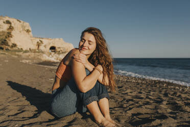 Lächelnde Frau auf Sand am Strand sitzend - DMGF01095
