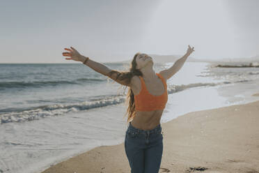 Carefree woman standing at beach with arms raised - DMGF01097