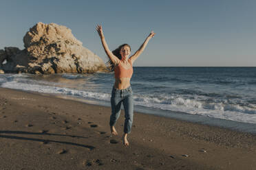 Cheerful woman jumping and running at beach - DMGF01100