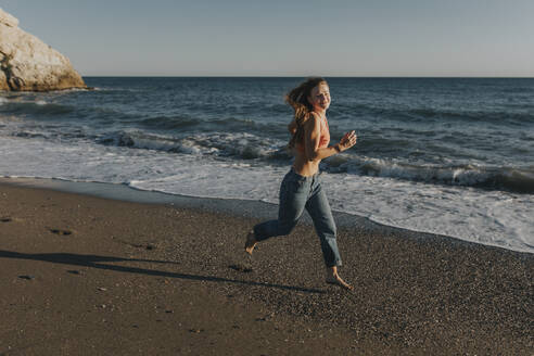 Happy woman running at beach - DMGF01101