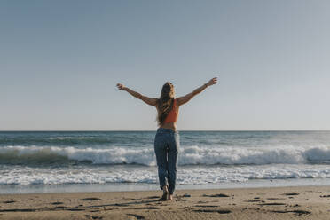 Carefree woman standing with arms outstretched in front of sea - DMGF01104