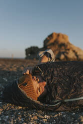 Frau mit Strickmütze im Schlafsack am Strand - DMGF01116