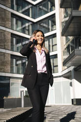 Smiling businesswoman talking on smart phone outside office building - AMWF01263