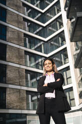 Smiling businesswoman standing with arms crossed outside office building - AMWF01265