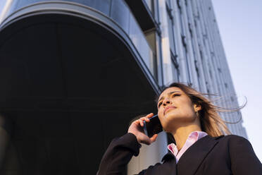 Geschäftsfrau, die in der Nähe eines Gebäudes mit einem Smartphone telefoniert - AMWF01276