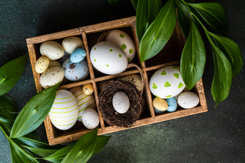 Von oben Frühling Ostern Holzkiste mit bunten Eiern und Nest von italienischen Ruscus Pflanze umgeben - ADSF43450