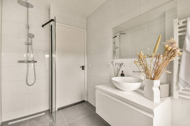 Contemporary bathroom interior with shower cabin and ceramic sink with mirror and decorative flowers in light apartment - ADSF43471