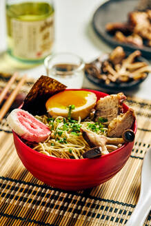 Von oben appetitliche Ramen-Suppe mit Fleisch und Ei und Nudeln in einer Schüssel auf dem Tisch neben Stäbchen und Glasbecher serviert - ADSF43478