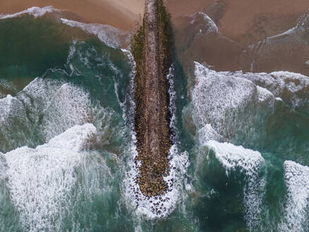 Luftaufnahme eines majestätischen Wellenbrechers mit rauen Wellen, die am Strand von Costa da Caparica, Setubal, Portugal, anrollen. - AAEF17680