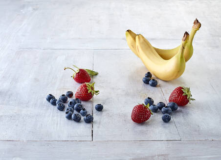 Frische Blaubeeren, Erdbeeren und Bananen auf einer weißen Fläche liegend - KSWF02337