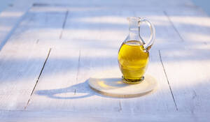 Krug mit Olivenöl auf Holzuntersetzer - KSWF02338