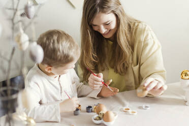 Happy mother and son decorating Easter eggs at home - ONAF00446
