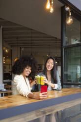 Happy friends toasting juices and taking selfie sitting at cafe - MMPF00688