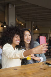 Zwei Freunde halten einen glücklichen Moment mit einem Selfie in einem gemütlichen Café fest - MMPF00690