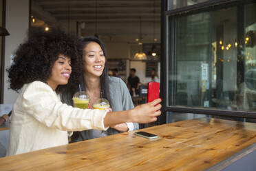 Zwei Freunde genießen ein gesundes Getränk in einem Café und halten den Moment mit einem Selfie fest - MMPF00692