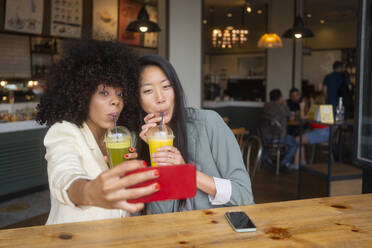 Freunde halten einen Moment der Gesundheit und des Glücks mit einem Selfie fest, während sie in einem Café an einem nahrhaften Saft nippen - MMPF00693