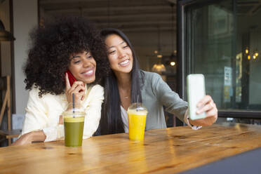 Zwei Freundinnen genießen die Gesellschaft des anderen in einem Café, wobei die eine ein Selfie macht und die andere mit ihrem Handy chattet - MMPF00696