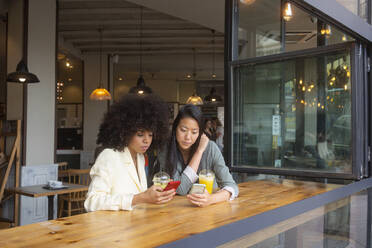 Freunde, die Smartphones benutzen, sitzen zusammen mit Saft in einem Café - MMPF00698