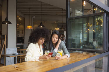 Friends using smart phones sitting together with juice at cafe - MMPF00698