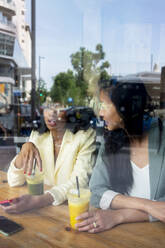 Friends talking to each other sitting in cafe seen through window - MMPF00703