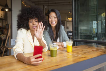 Frauen führen einen Videoanruf mit einem Smartphone im Café - MMPF00707