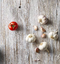 Garlic cloves and single tomato lying on wooden surface - KSWF02348