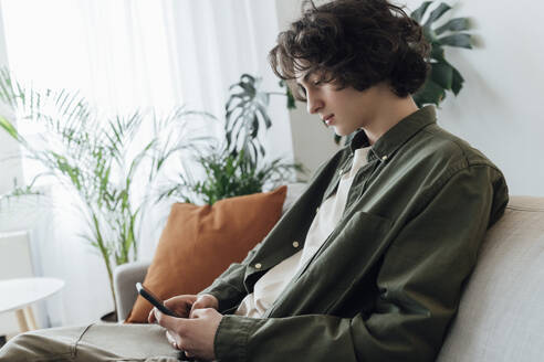 Junge mit langen Haaren benutzt Smartphone zu Hause - AAZF00232