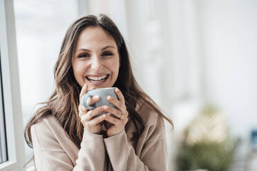 Glückliche junge Frau hält Kaffeetasse zu Hause - JOSEF17661