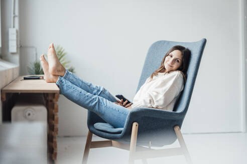 Lächelnde Frau im Sessel sitzend mit hochgelegten Füßen zu Hause - JOSEF17684