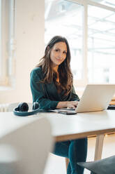 Smiling businesswoman sitting with laptop at home office - JOSEF17688