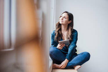 Smiling thoughtful freelancer sitting with tablet PC at home office - JOSEF17708