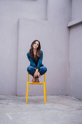 Junge Frau sitzt auf einem gelben Stuhl vor einer Wand - JOSEF17731