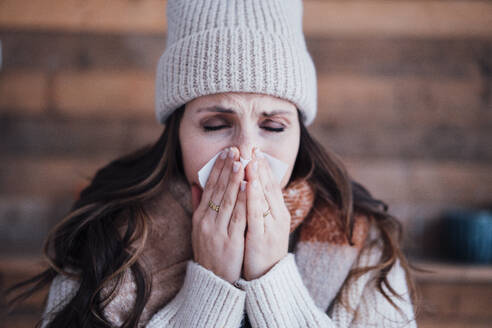 Sick woman wearing knit hat blowing nose - JOSEF17746