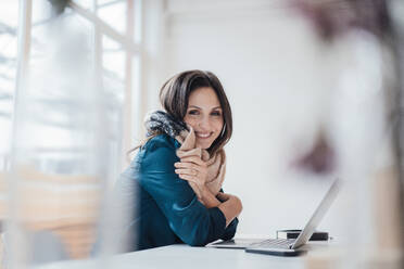 Happy businesswoman sitting with laptop on table at home office - JOSEF17755