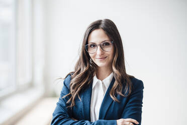 Smiling businesswoman wearing eyeglasses standing at home office - JOSEF17773