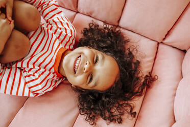 Happy girl having fun on pink sofa at home - MDOF00896