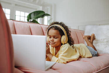 Girl wearing wireless headphones studying on laptop at home - MDOF00909