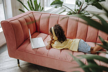 Mädchen liegt auf dem Sofa und studiert mit Laptop zu Hause - MDOF00911