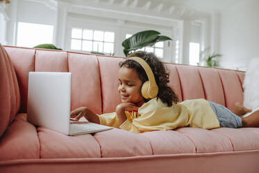 Smiling girl lying on sofa and studying through laptop in living room at home - MDOF00913