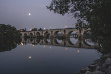 Spain, Castilla y Leon, Zamora, Puente de Piedra bridge reflecting in Douro river at dusk - KEBF02654