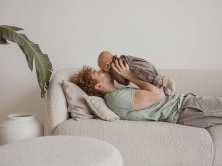 Father kissing son lying on sofa at home - MFF09298