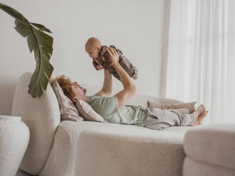 Father lying on sofa and playing with son at home - MFF09299