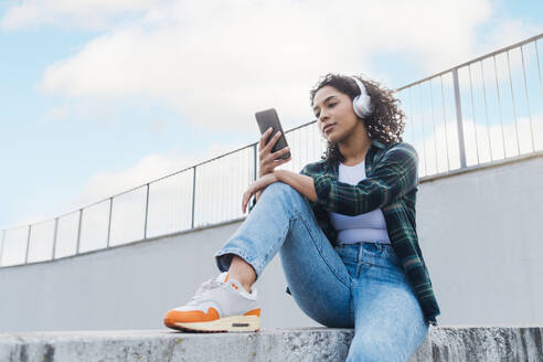 Young woman wearing wireless headphones using smart phone - MEUF08951