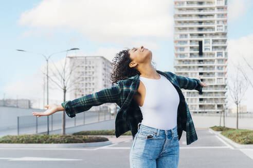 Carefree young woman with arms outstretched standing on parking lot - MEUF08957